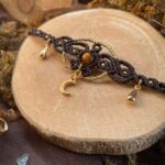 Collier ras de cou en micro macramé avec petites feuilles en dessous. Perles dorées, petite Lune en pendentif en dessous. Perle en pierre d'oeil de tigre en centre. Breloques gouttes sur les côtés.